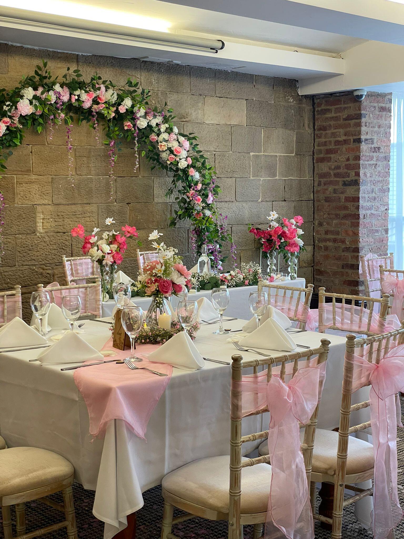 A function room with stone and brick walls, floral centerpieces, and pink-accented table settings at The Garrison Hotel.