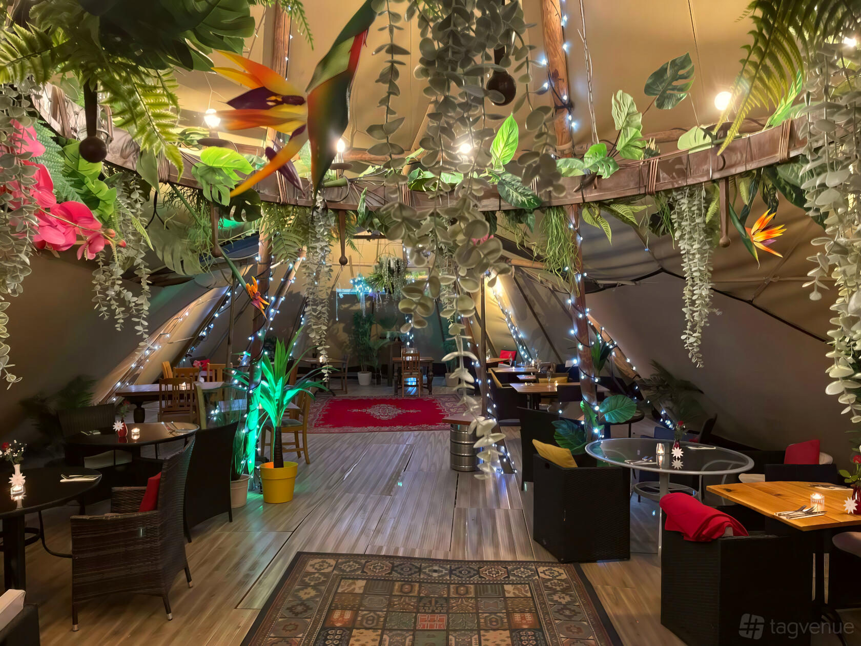 An event space in a pub with hanging greenery, string lights, and scattered tables inside a tipi at The Moody Mare.
