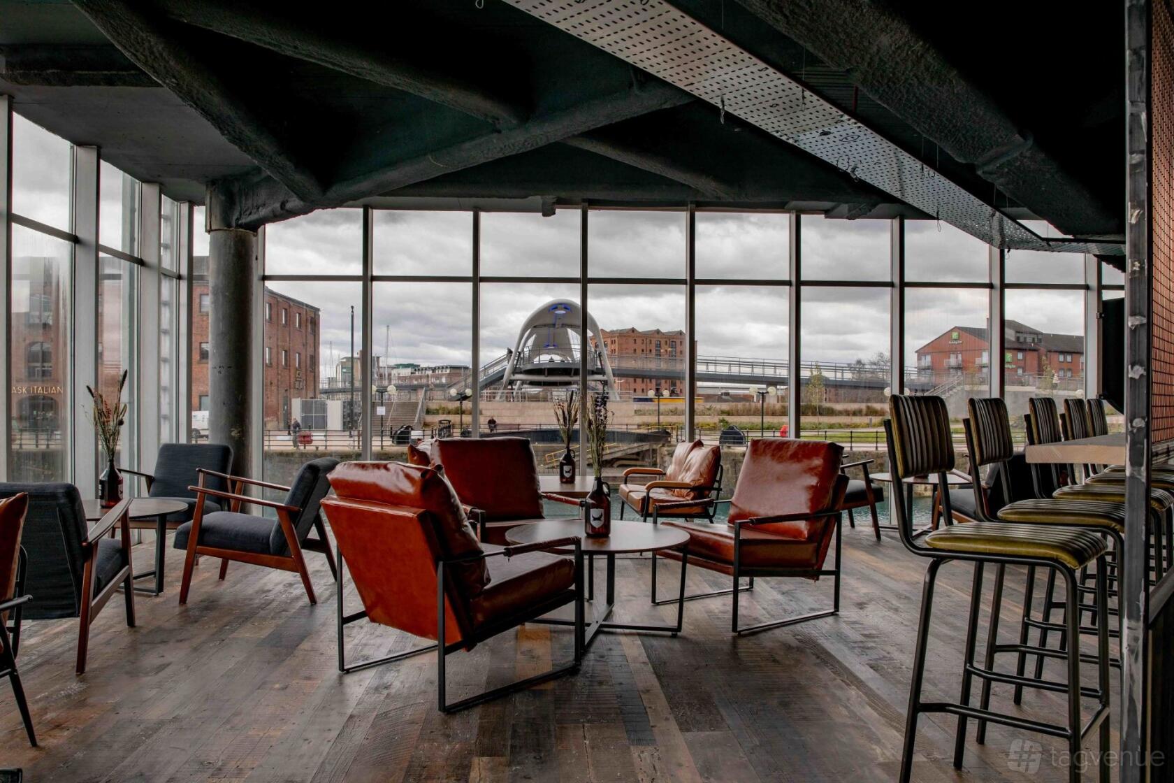 An event space in a bar with floor-to-ceiling windows, leather armchairs, and wooden flooring at BrewDog Hull.