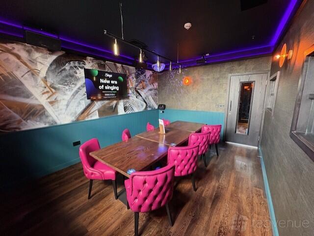 A karaoke room in a bar with pink velvet chairs, a flat-screen TV, and accent purple lighting at Manahatta York.