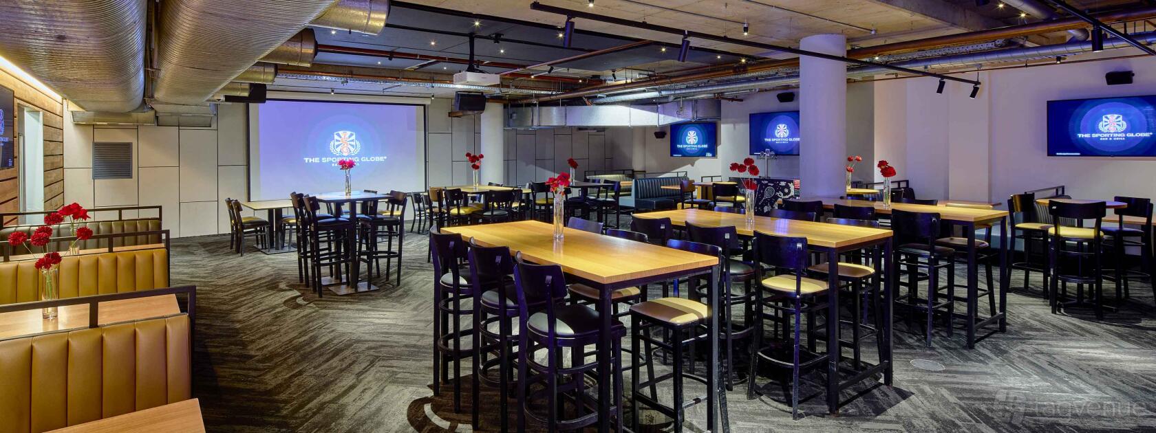 An event space in a pub with high wooden tables, black bar stools, red flower centerpieces, and large projector screens at The Sporting Globe King Street Wharf.