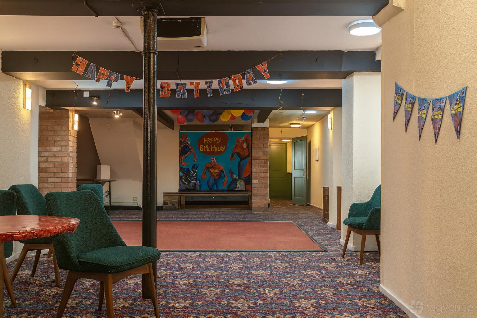 A function room in a pub with colorful carpeting, green chairs, and birthday decorations at The Garden Bar at Bridgnorth Club.