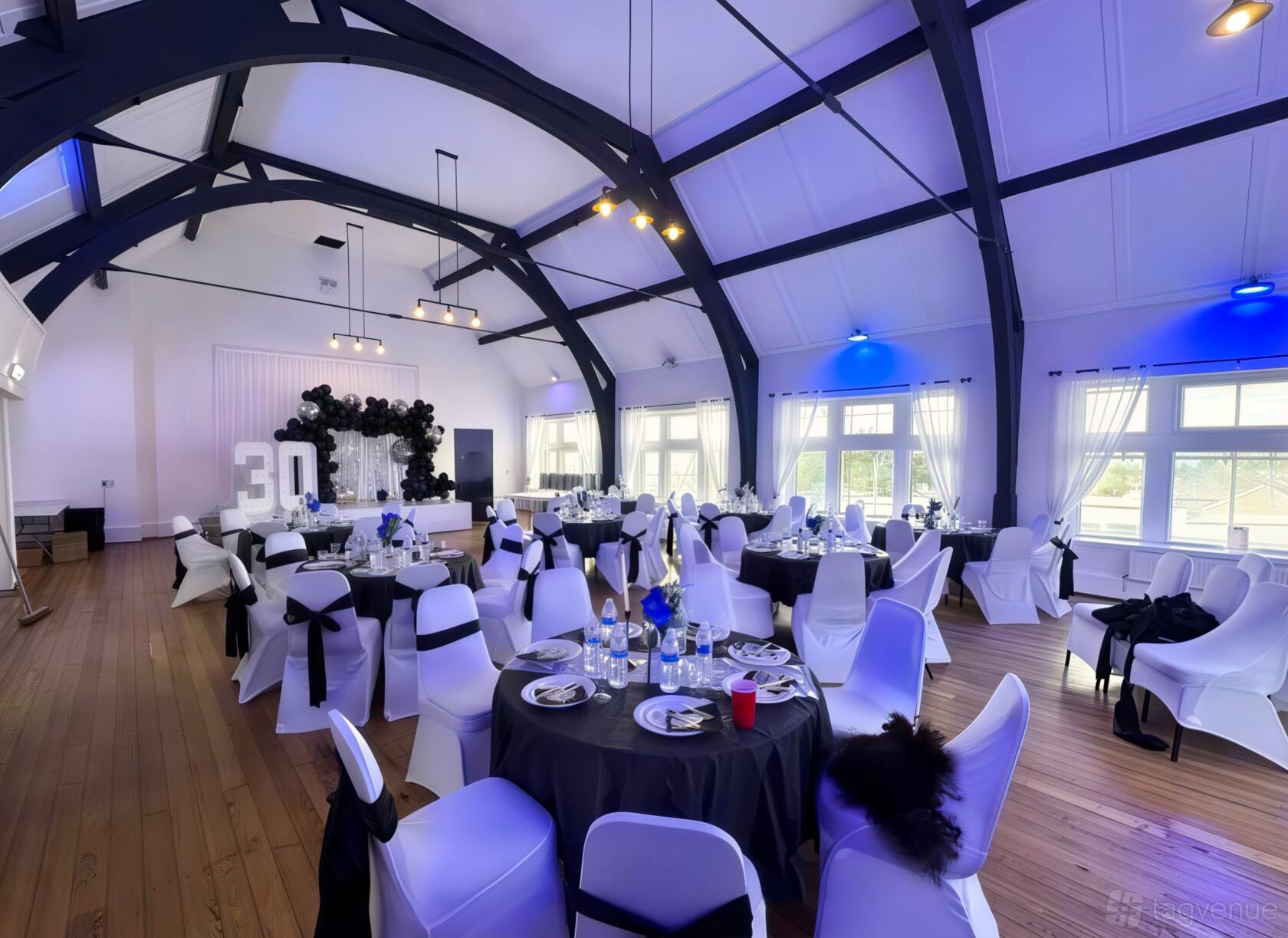 An event venue with arched ceilings, large windows, and round tables with black and white décor at Signature Suites.