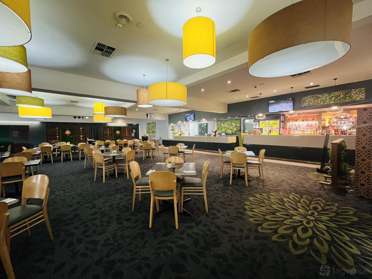 A hotel dining room with wooden chairs, round tables, patterned carpeting, and large yellow pendant lights at Westside Hotel.