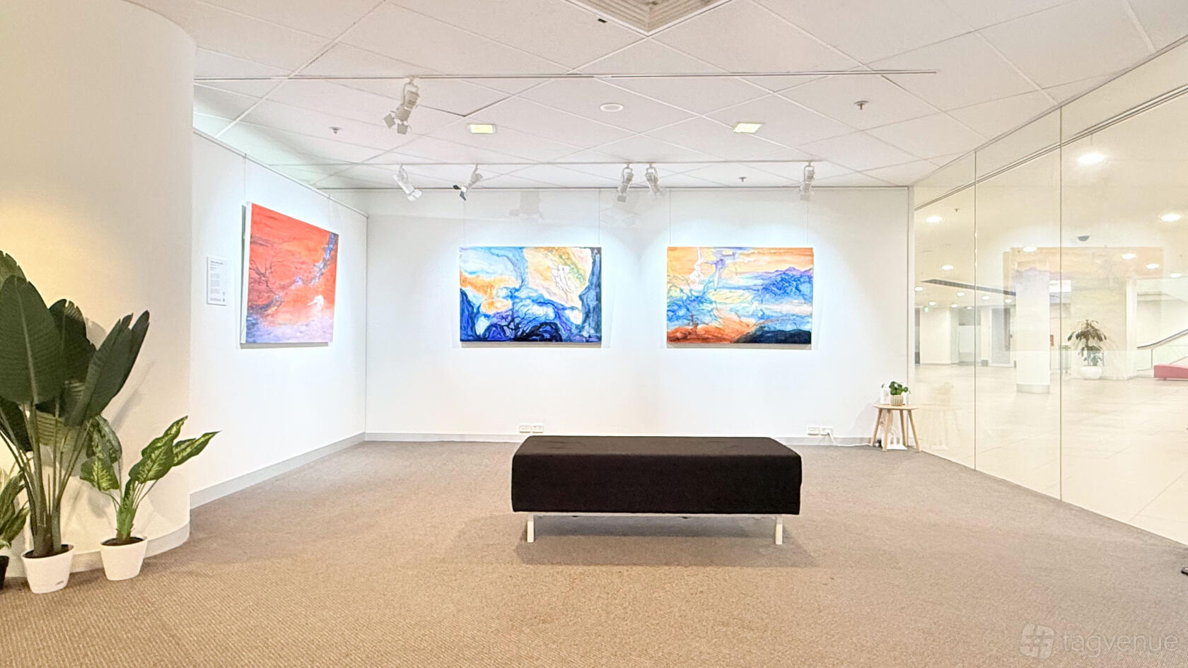 An art gallery with abstract paintings, track lighting, a black bench, and glass walls at Creative Asia Art Centre.
