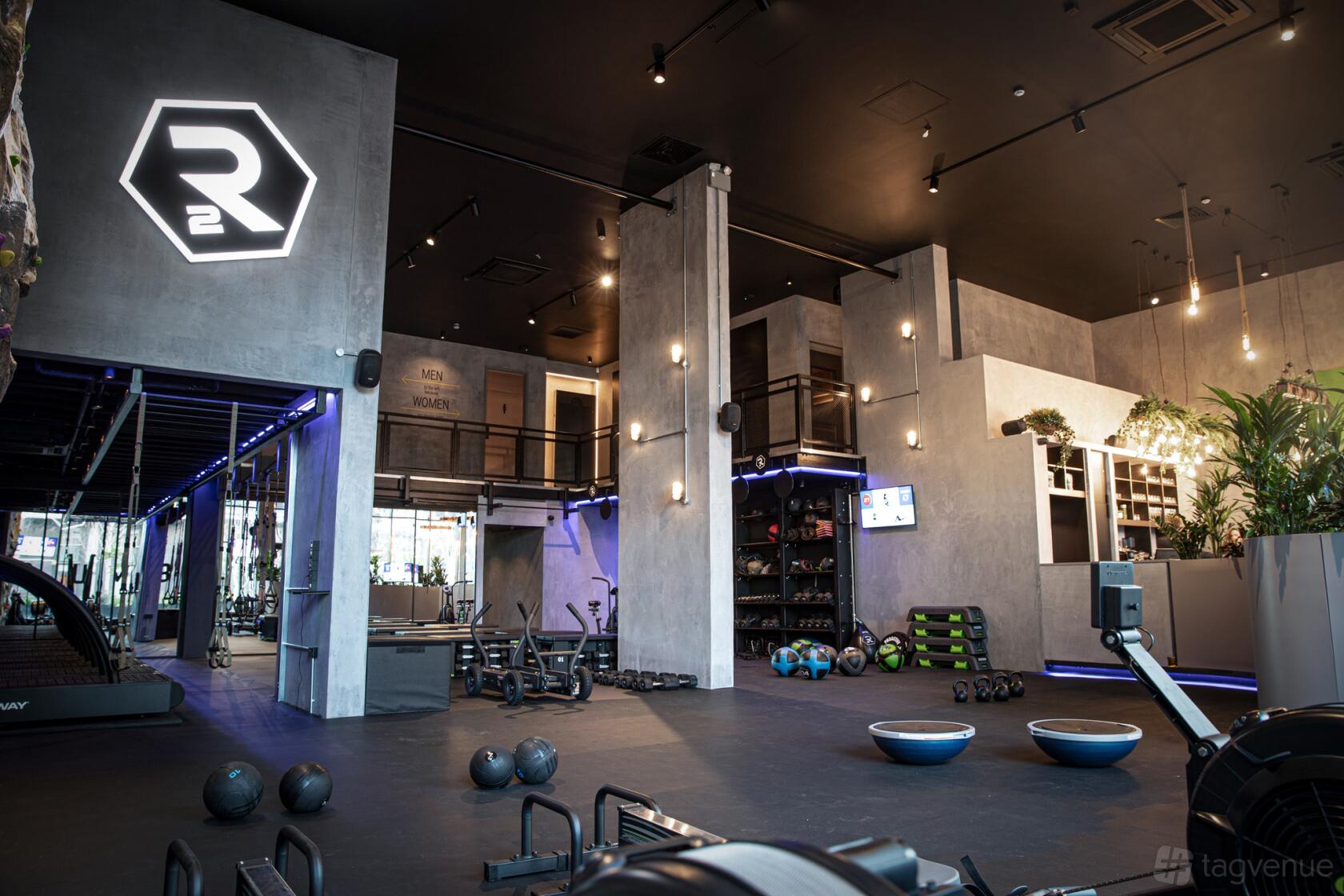 A loft fitness studio with exposed concrete pillars, exercise equipment, and neon signage at RUMBLE.