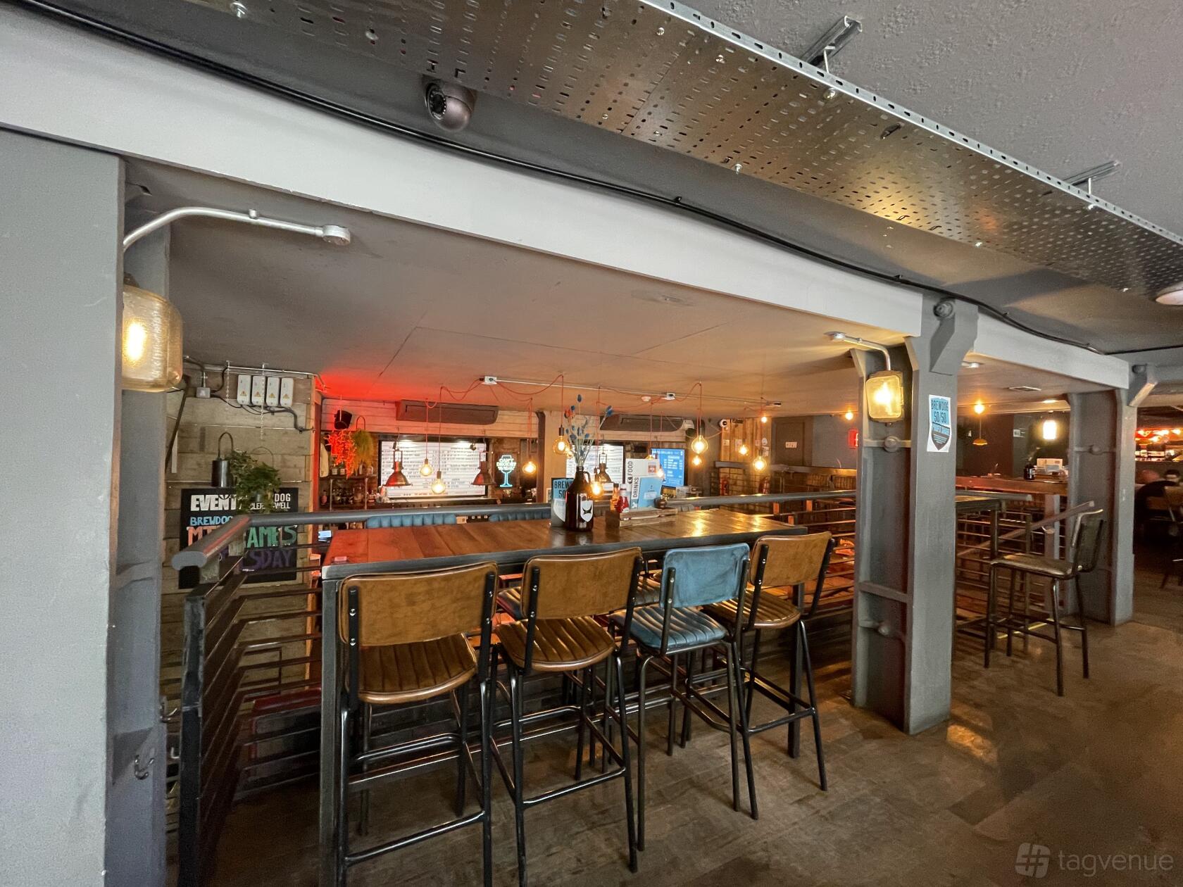 An event space in a bar with high tables, metal stools, and exposed ceiling at BrewDog Clerkenwell.