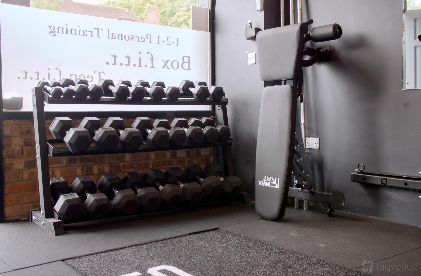 A fitness studio with a rack of free weights and an adjustable bench by large windows at F.I.T.T studio.