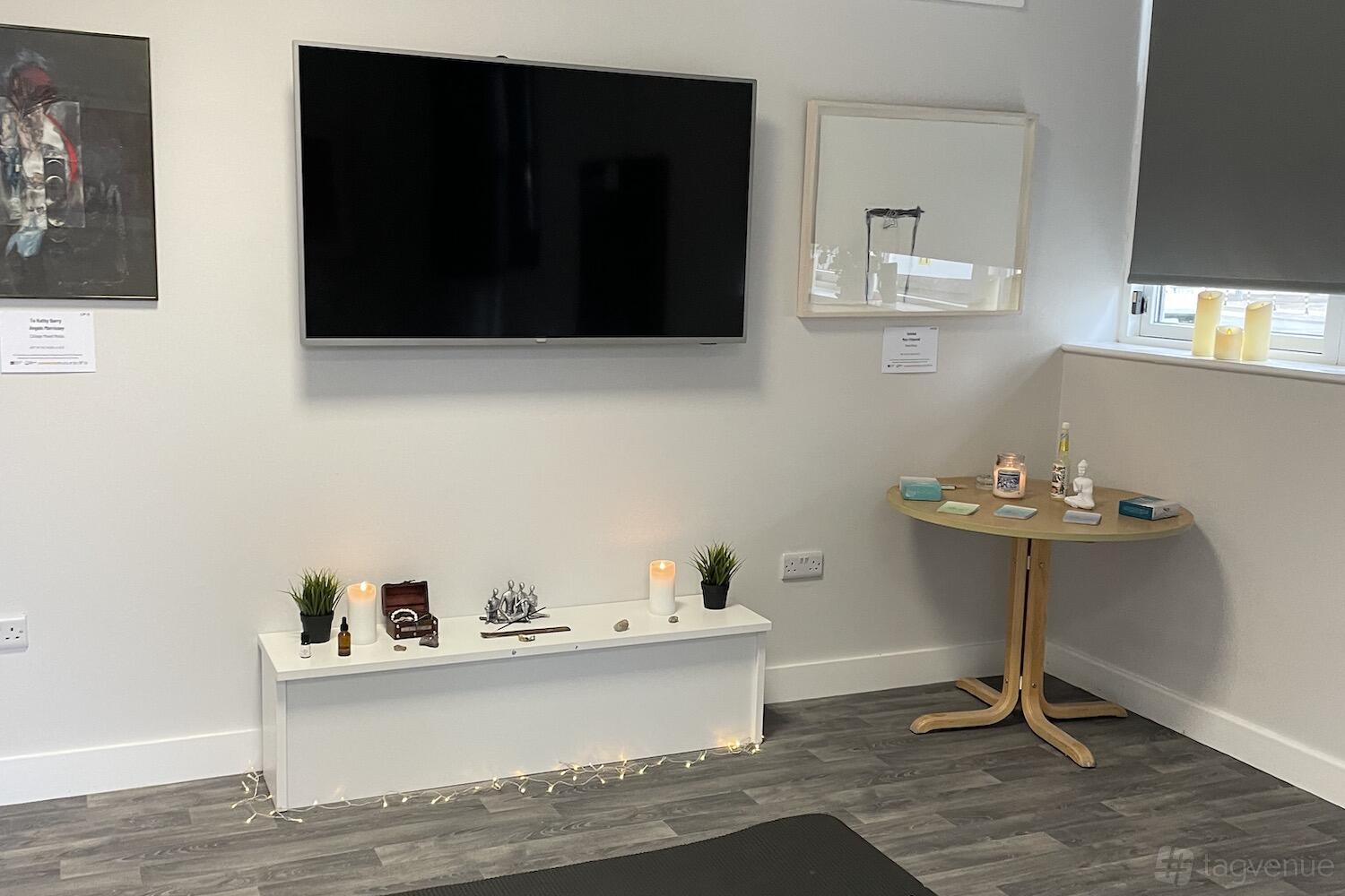 A training room with a wall-mounted TV, small plants, decorative candles, and a round wooden table at ACE Enterprise Park.