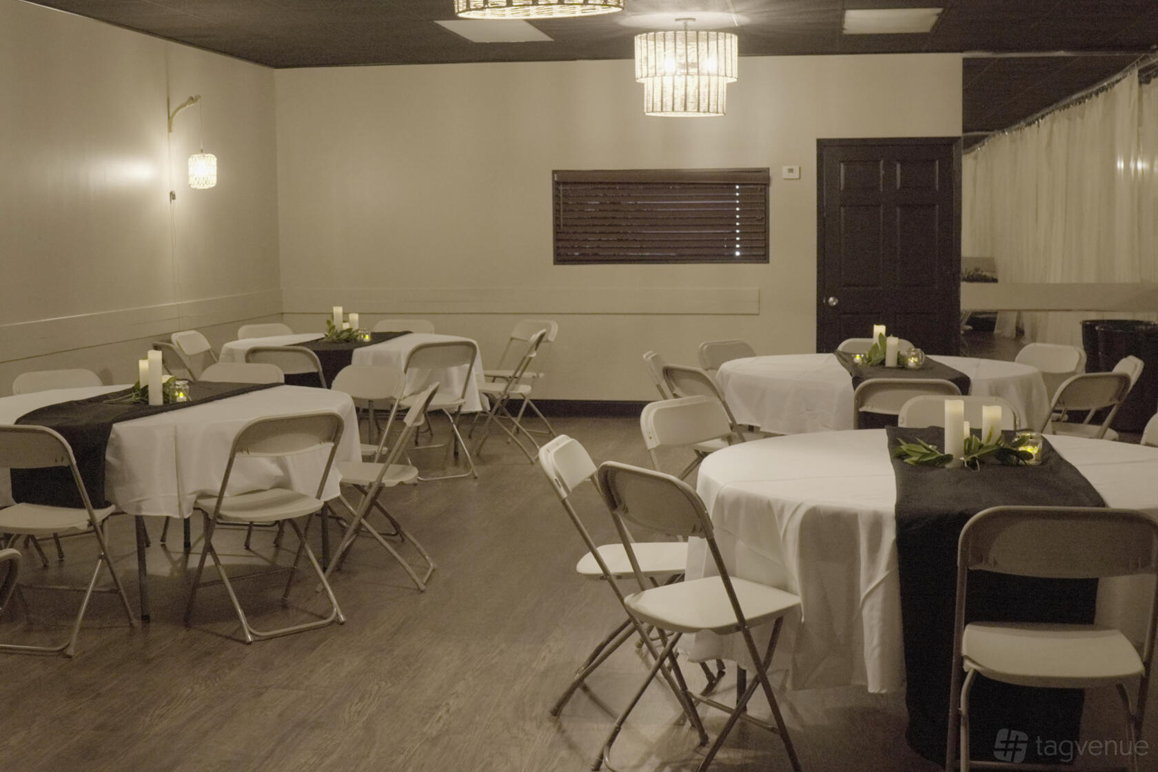 A hall with round tables covered in white linens, black table runners, and folding chairs at The Hive.