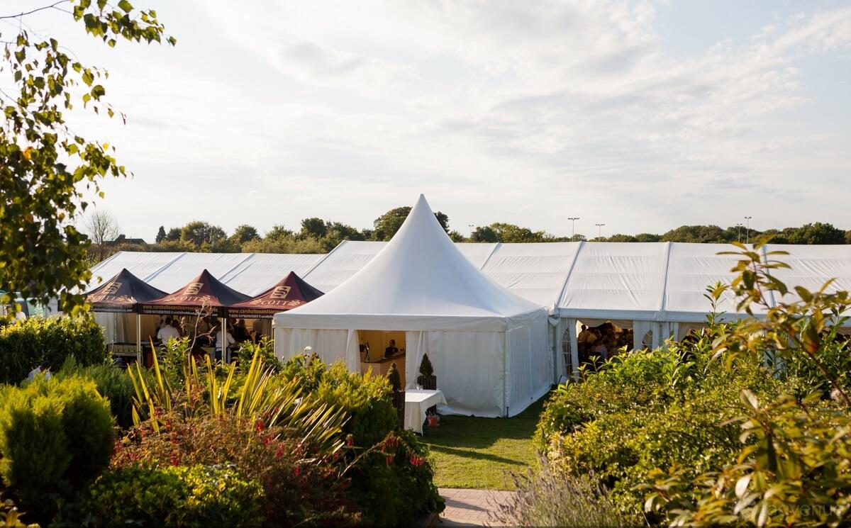 A versatile event space with a large white marquee tent surrounded by landscaped greenery at Zinnia Gardens.