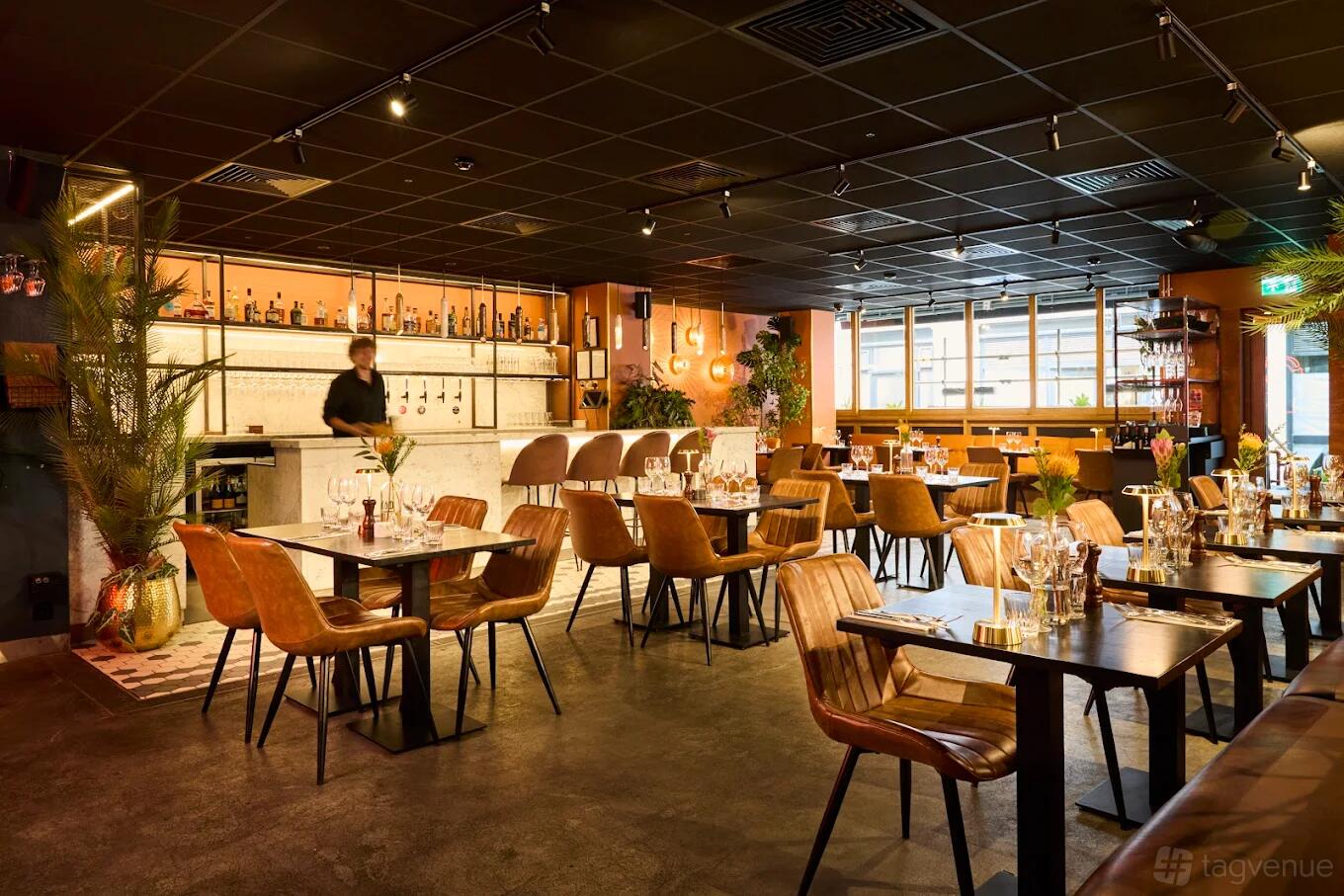 A restaurant with wooden tables, brown leather chairs, and a marble bar counter at KöD Soho.