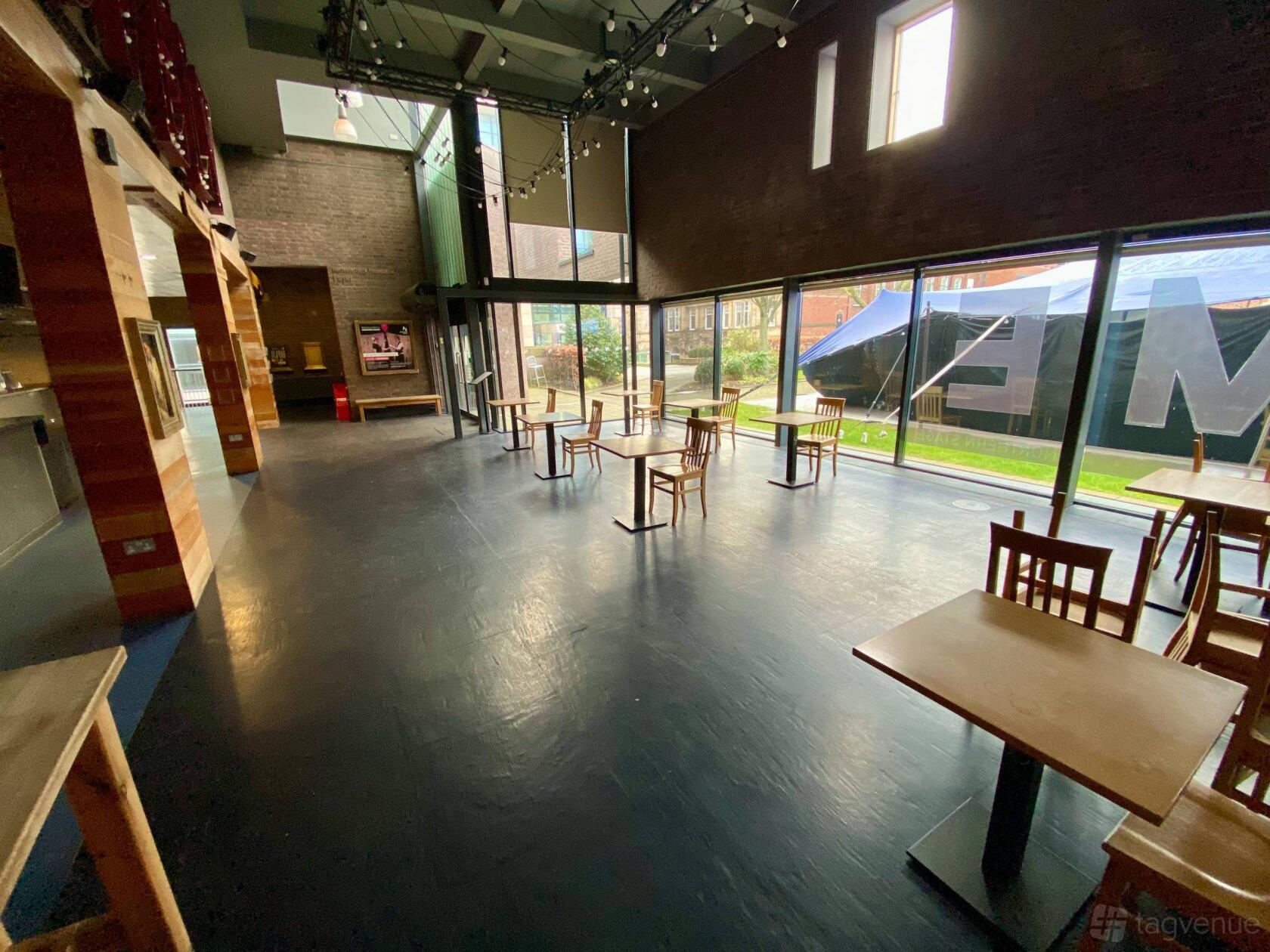 A cafe with floor-to-ceiling windows, wooden tables and chairs, and open floor space at The Northern Stage.