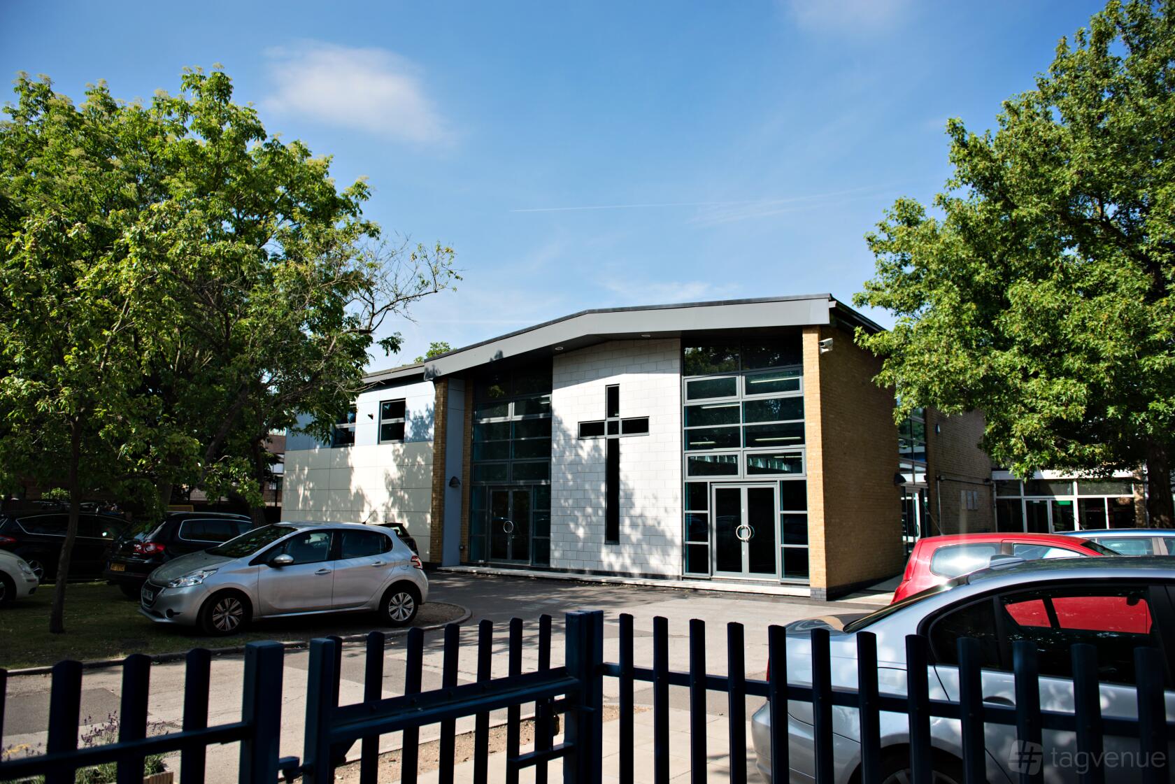 A school hall building with large glass windows, brick walls, and surrounding trees at The Blue school hall.