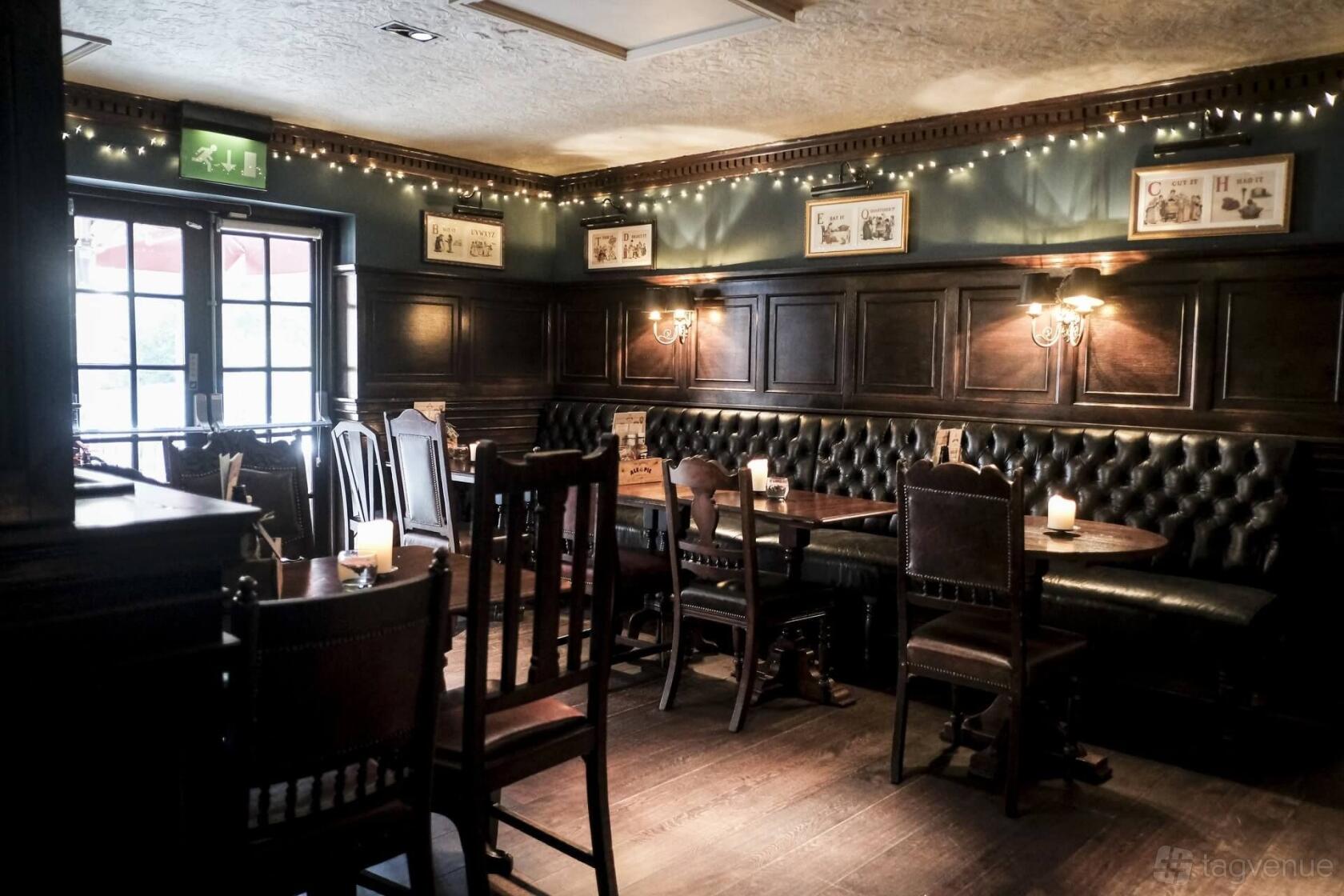 A pub dining room with tufted leather banquette seating, dark wood paneling, and wall sconces at The Partridge, Bromley.