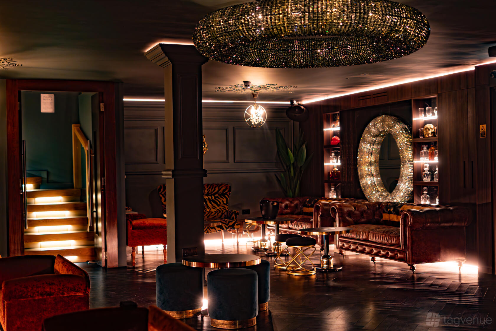 A cocktail bar with dark wood floors, velvet seating, and a large illuminated mirror at Living Room At The Chiswick.