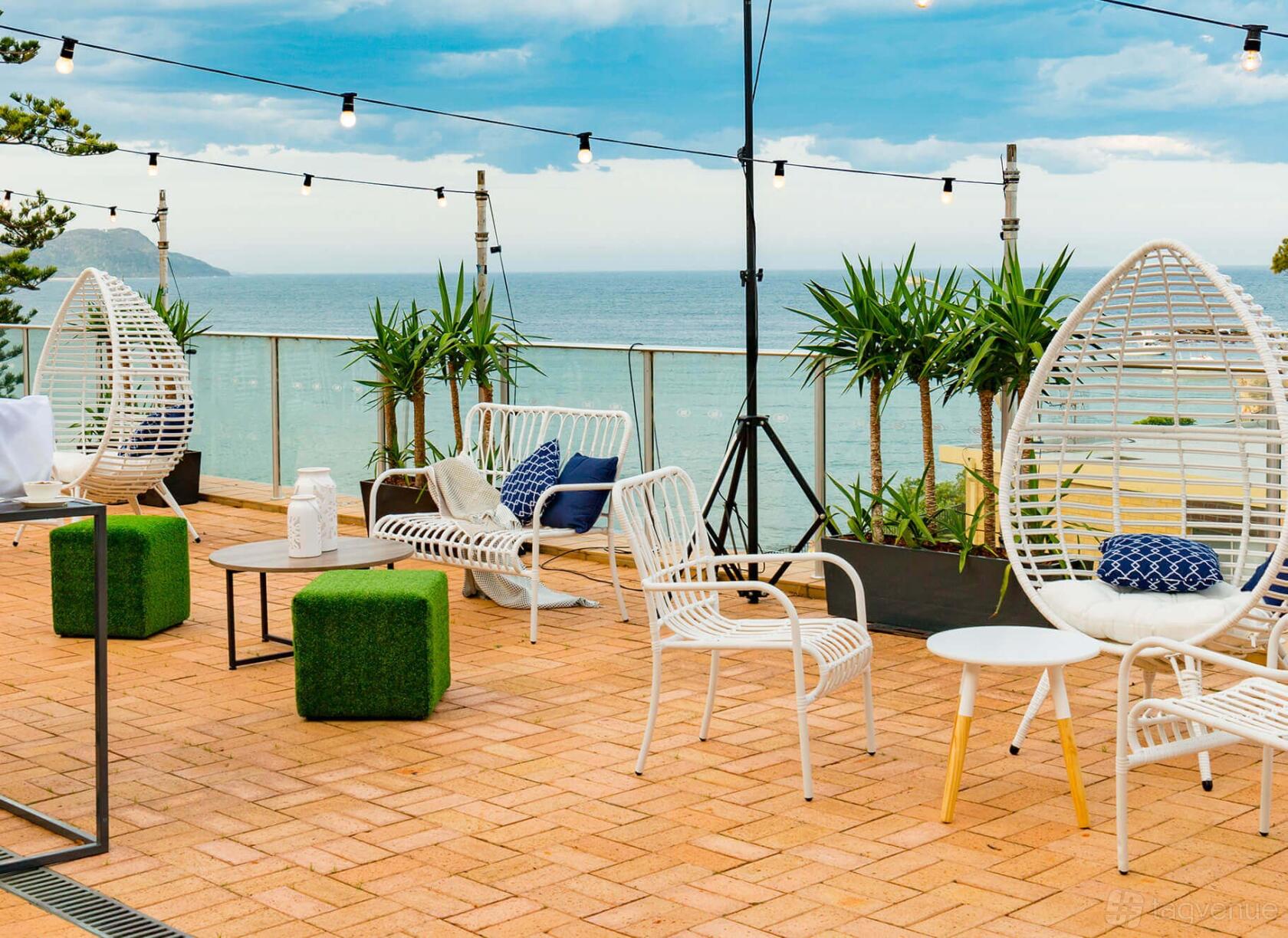 An event space with wicker lounge chairs, string lights, ocean views, and potted plants at Crowne Plaza Terrigal Pacific.