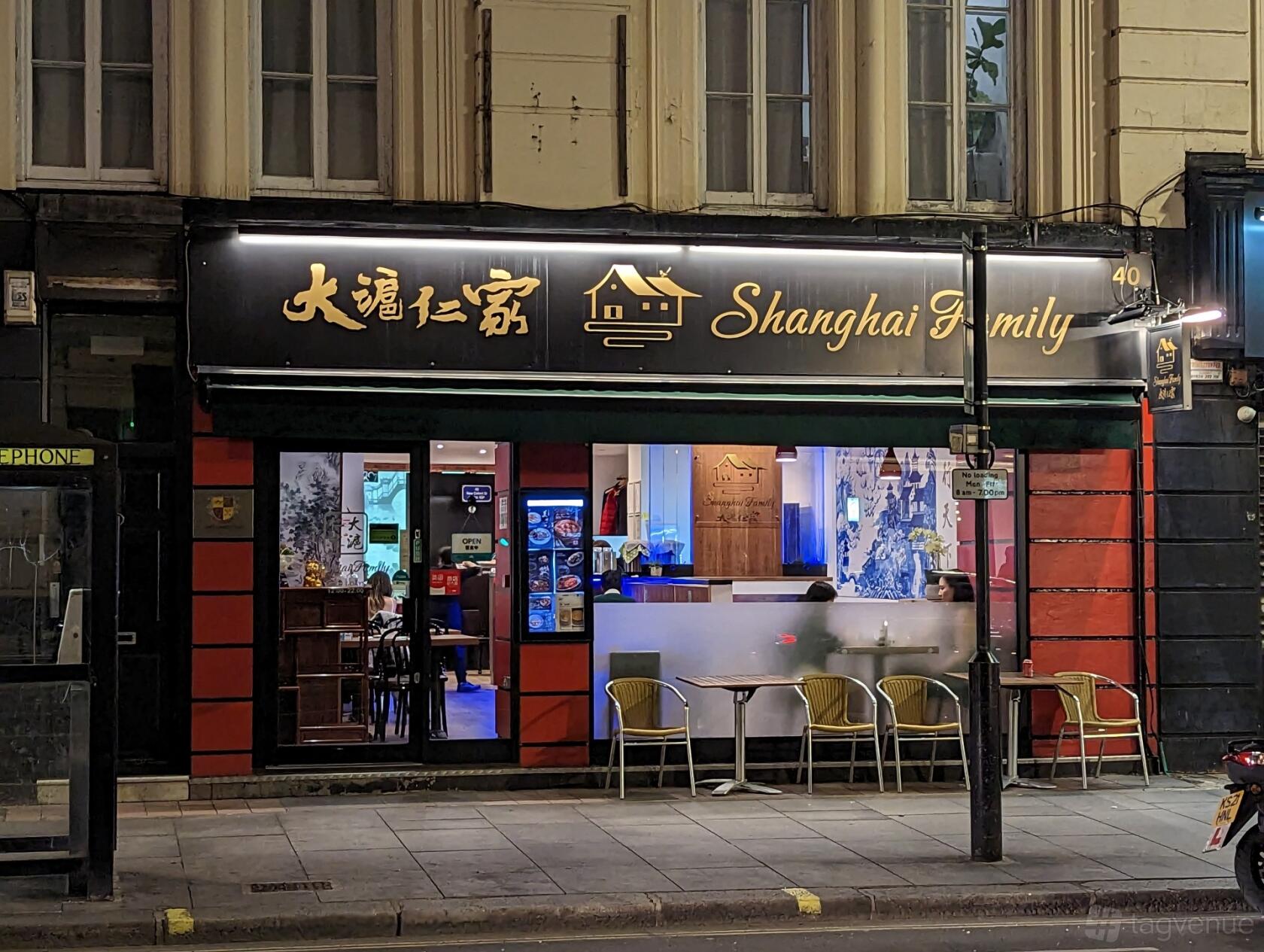 A restaurant with illuminated signage, red panel exterior, and outdoor seating at Shanghai Family.