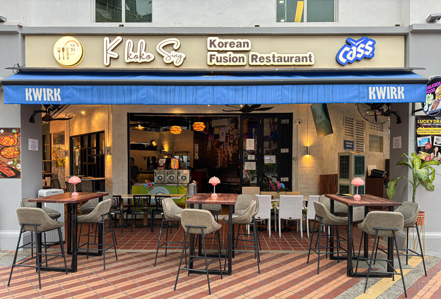 A restaurant with outdoor high tables and barstool seating under a blue awning at Kkoko Sing Korean Fusion Restaurant.