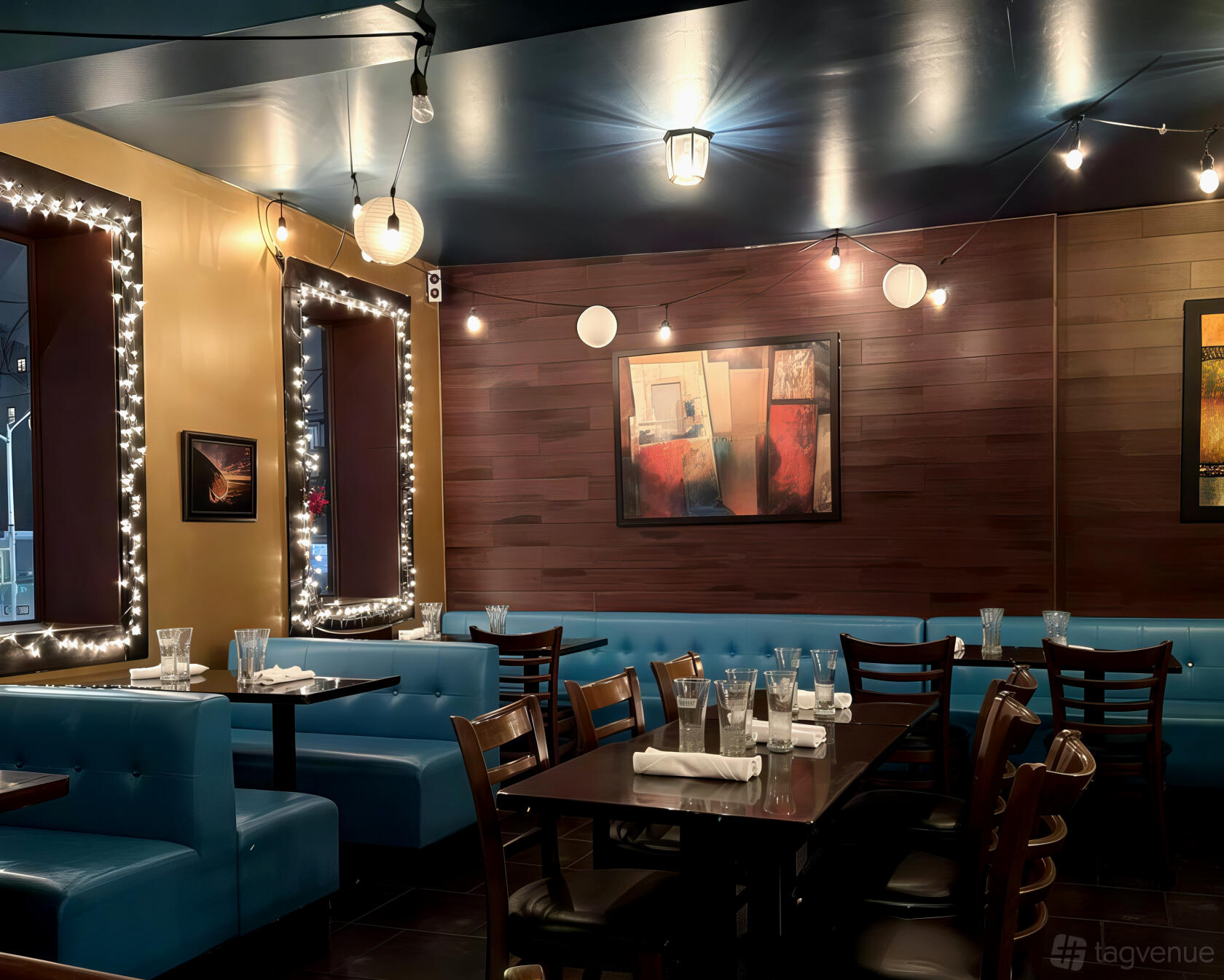 A dining room with blue upholstered booths, string lights, and framed artwork at Surfish Bistro.
