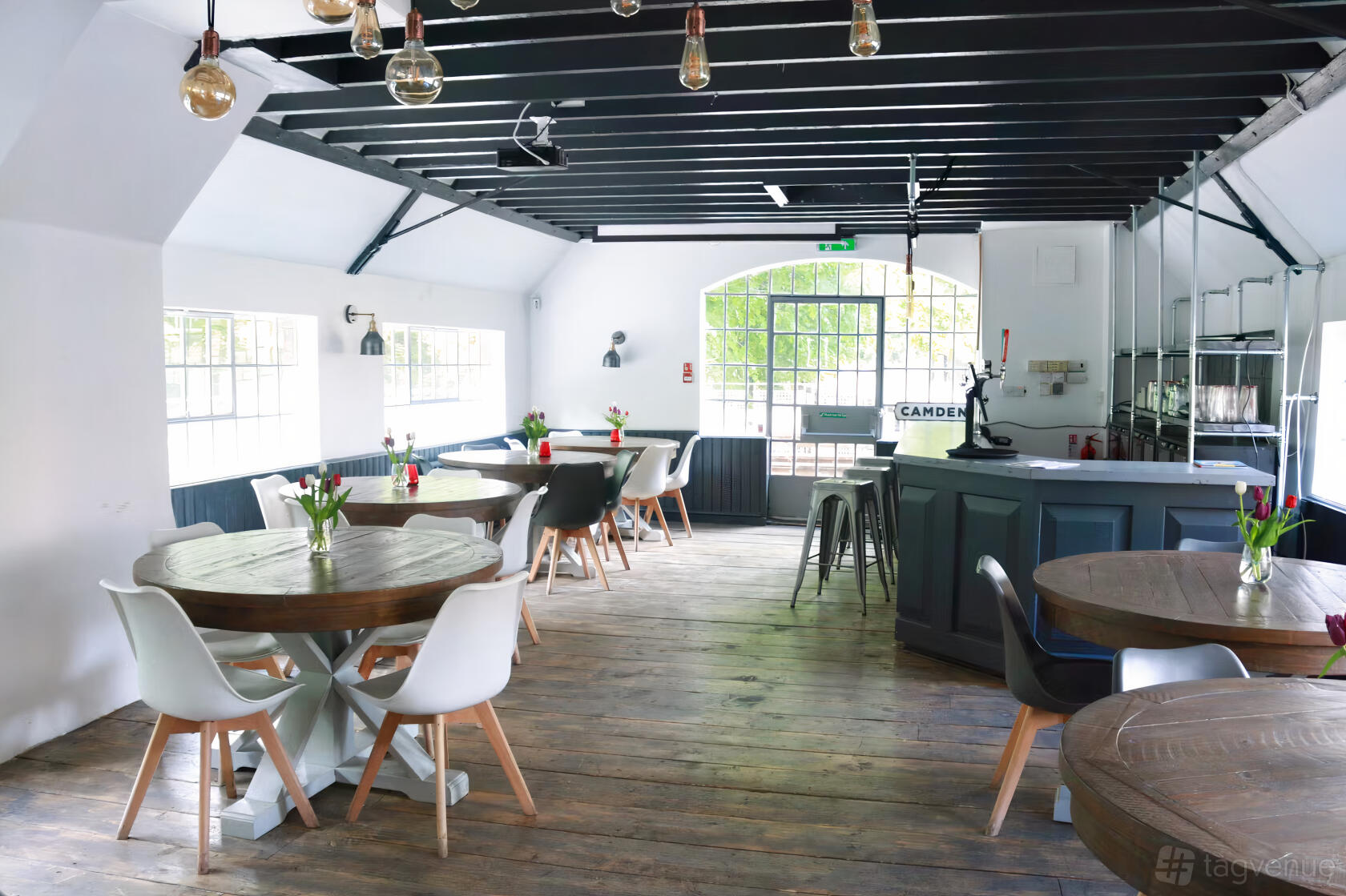 An event space in a pub with wooden floors, round tables, and large windows at The William Morris.