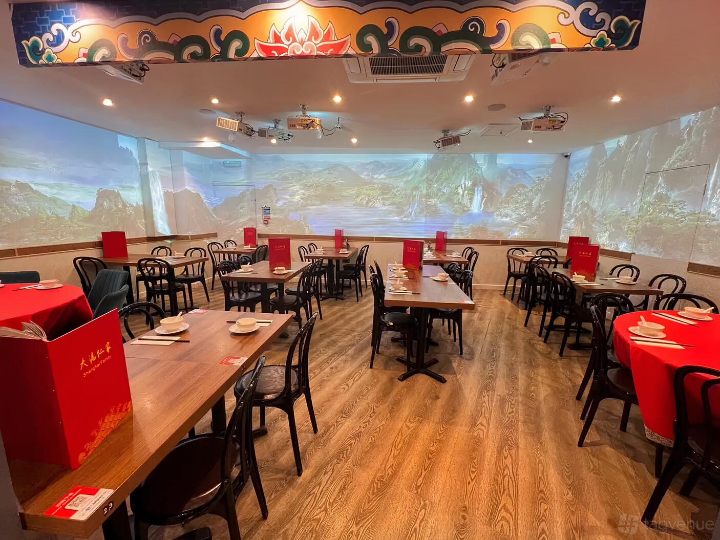 An event space in a restaurant with wood floors, scenic wall projections, and tables set for dining at Shanghai Family.