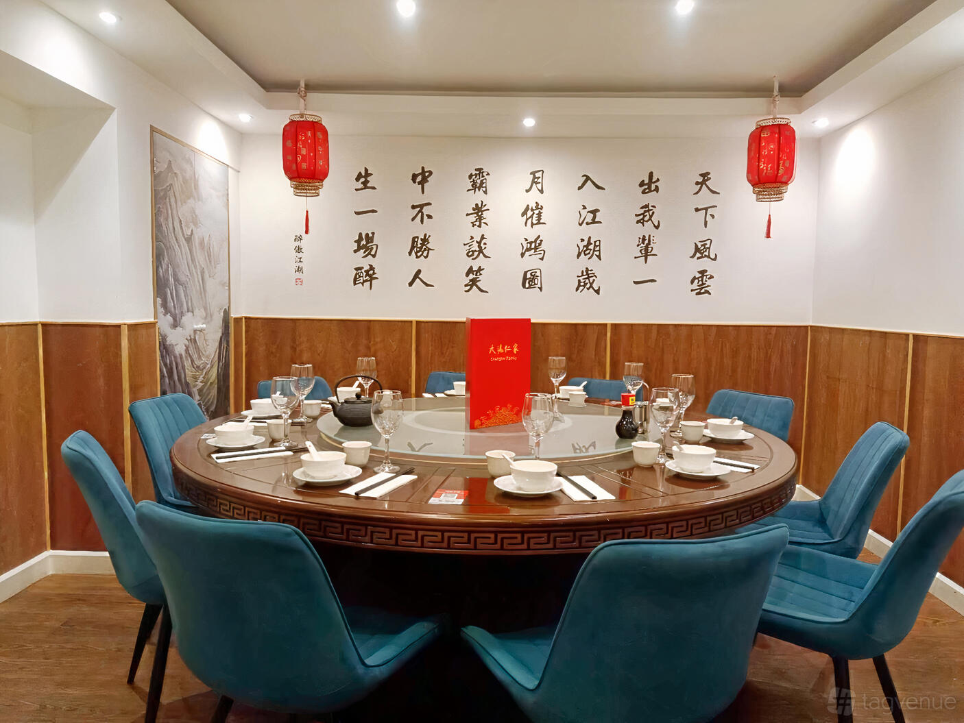 A restaurant dining room with a round table set for eight, teal chairs, red lanterns, and Chinese calligraphy at Shanghai Family.