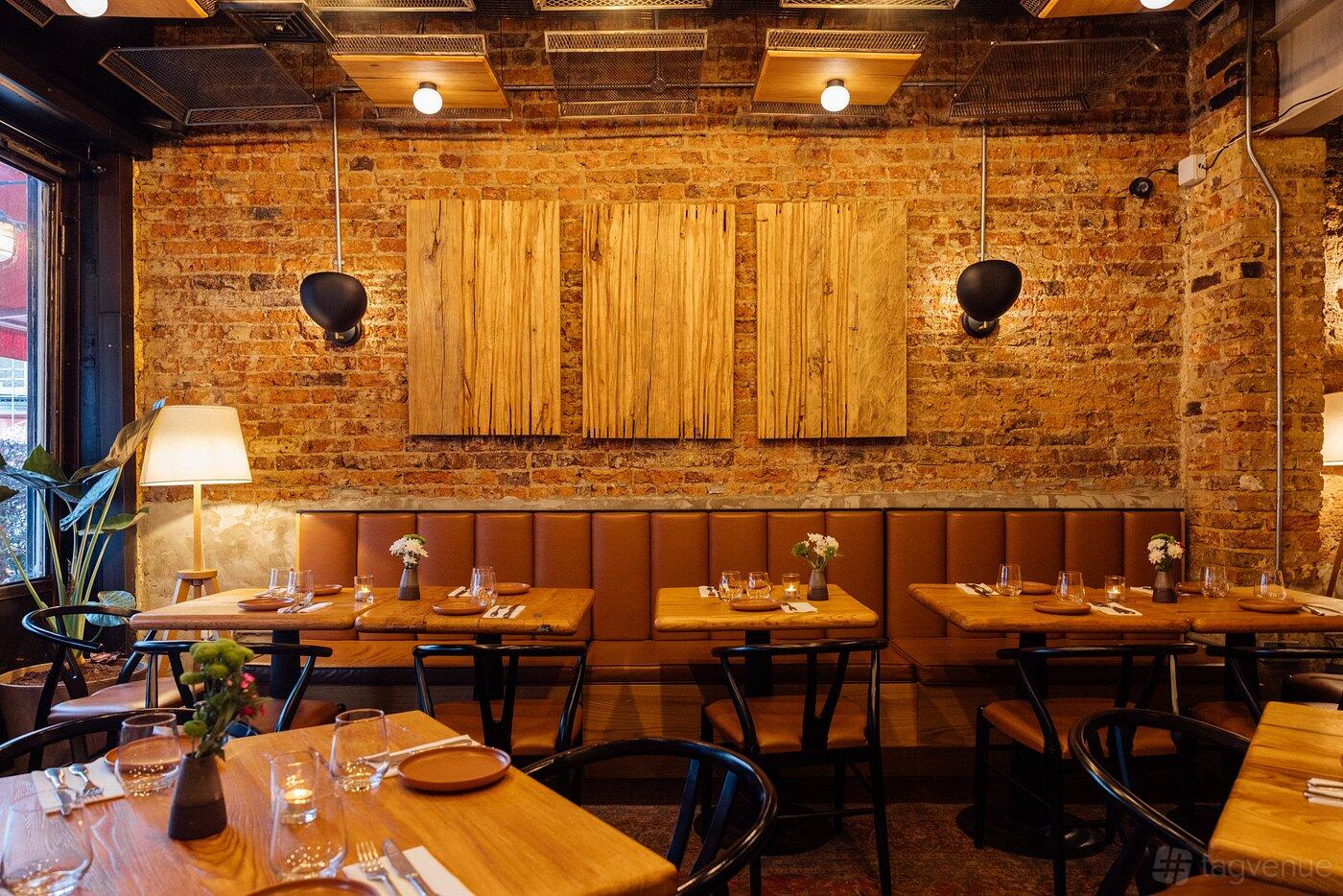 A restaurant with exposed brick walls, wood panel decor, and wooden tables set for dining at The Counter - Notting Hill.