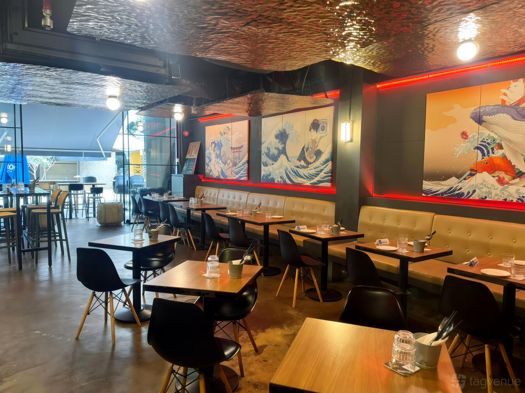 An event space with booth seating, black chairs, wall art, and red accent lighting at Miss G Grill & Bar.