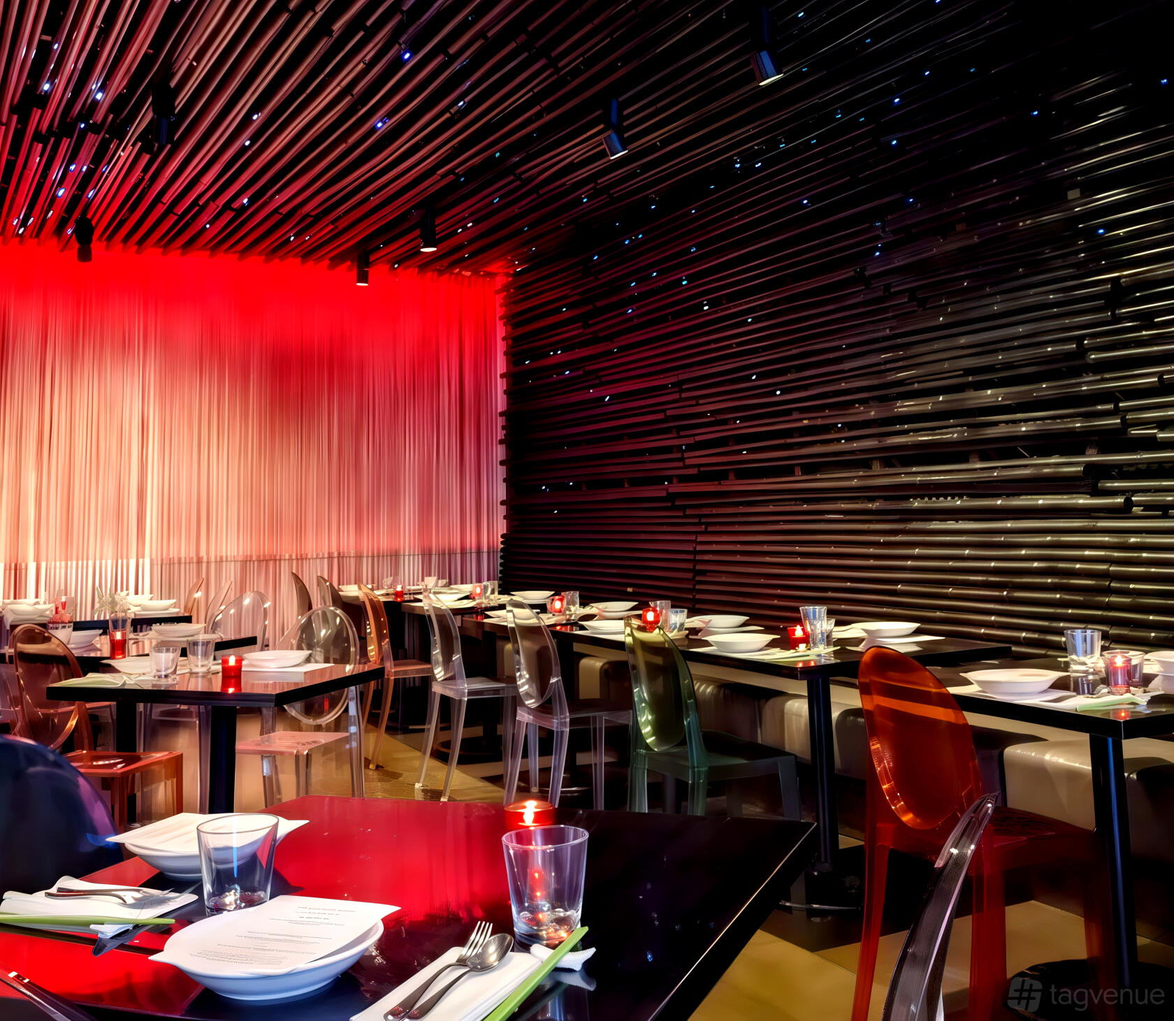 An event space in a restaurant with transparent chairs, modern black tables, and a dramatic red-lit wall at Chapati.