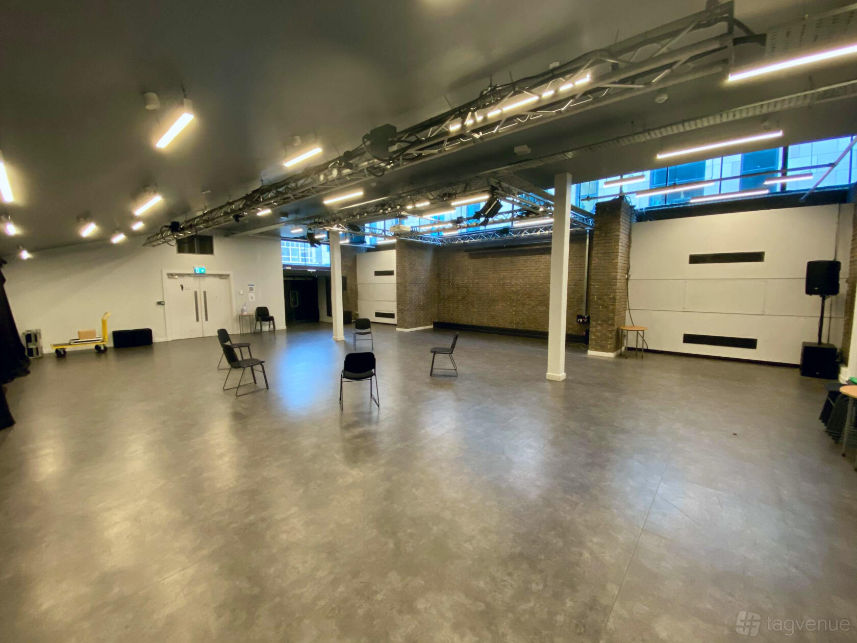 An auditorium with exposed ceiling fixtures, brick accent wall, and scattered chairs at The Northern Stage.