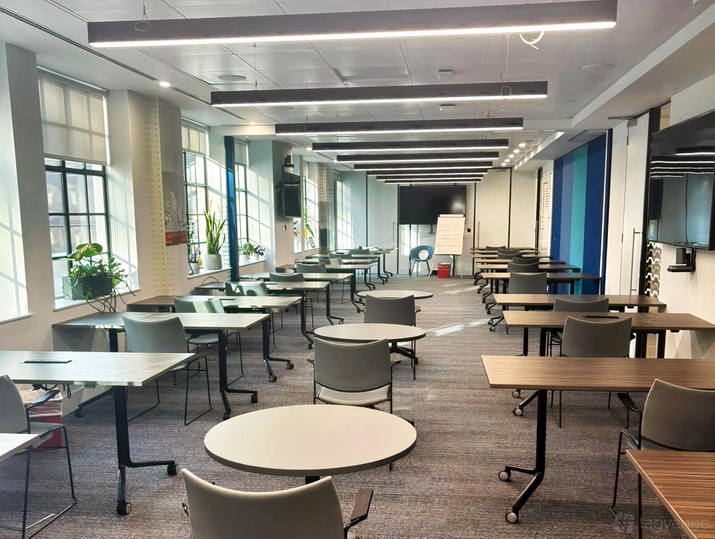 A meeting room with individual tables, gray chairs, large windows, and potted plants at ICS Maritime Hub.