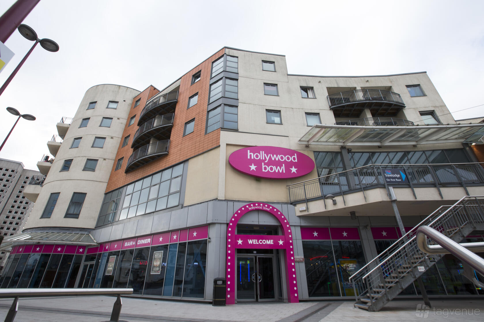 An exterior view of Hollywood Bowl Birmingham Broadway Plaza with pink signage and modern building facade.