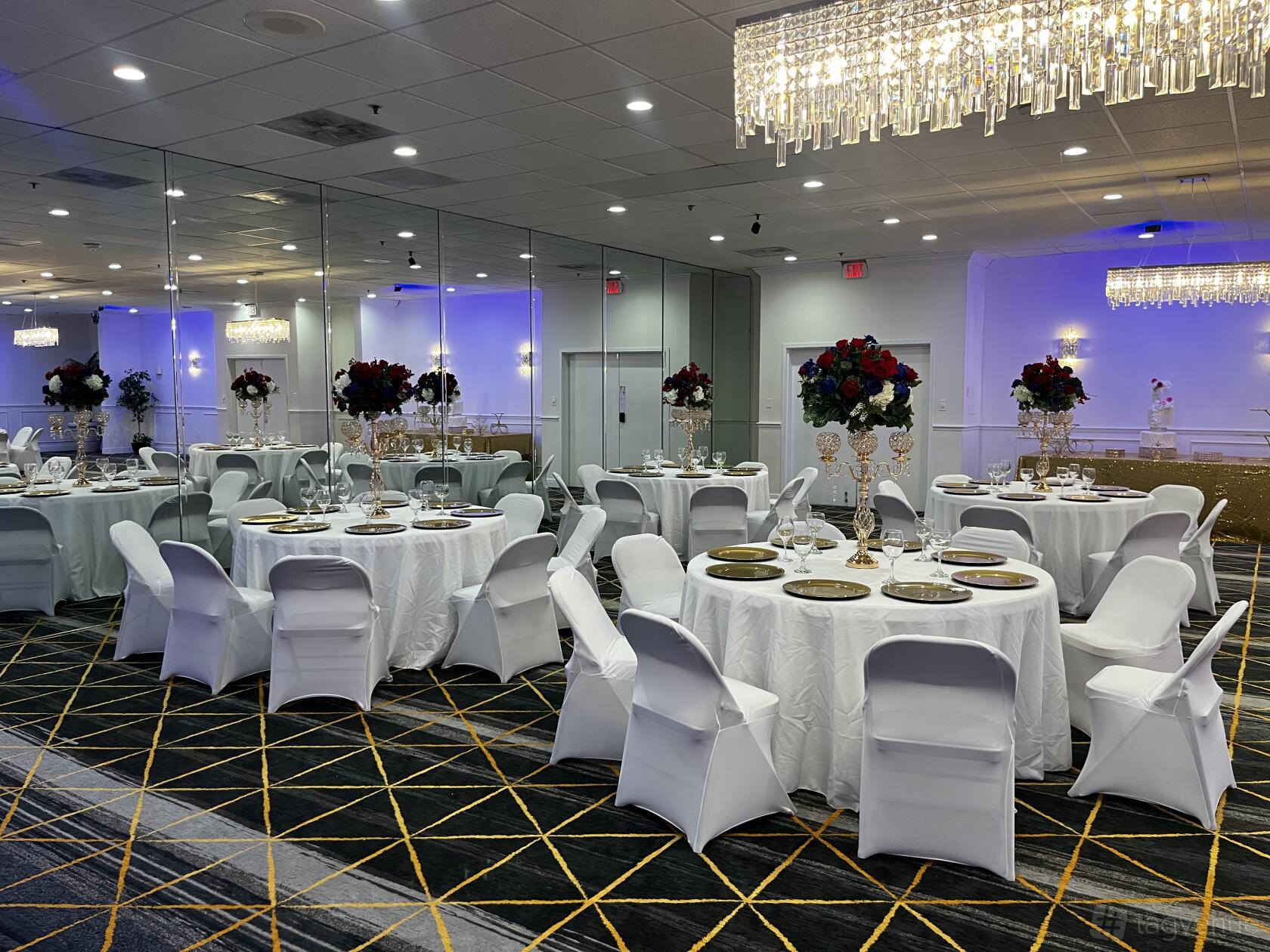 A ballroom with round tables draped in white linens, gold chargers, mirrored walls, and crystal chandeliers at The View Event Venue.