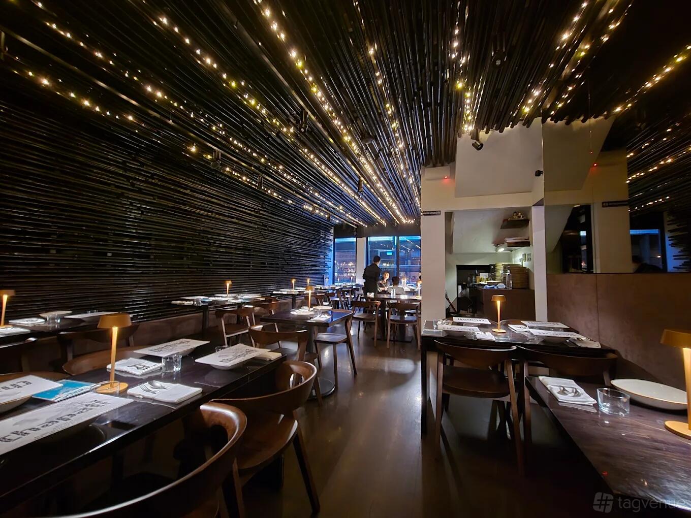 A bar in a restaurant with warm lighting, wooden tables, and a ceiling covered in bamboo and string lights at Chapati.