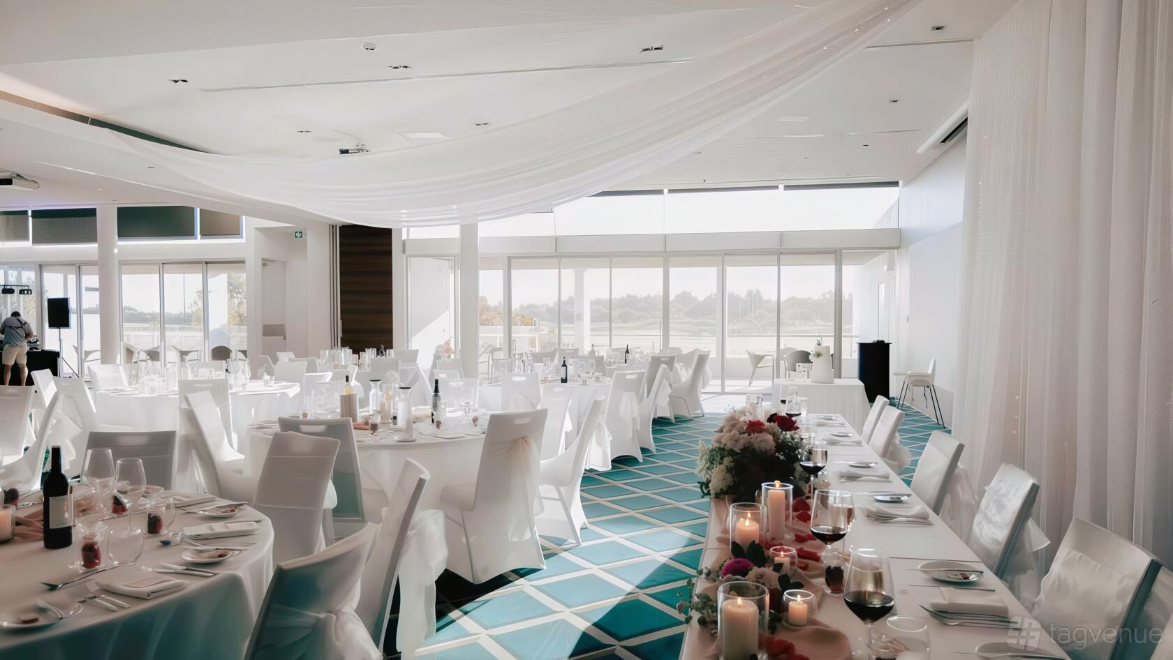 An auditorium with floor-to-ceiling windows, white draped ceilings, and round tables with white linens at Pullman Magenta Shores Resort.