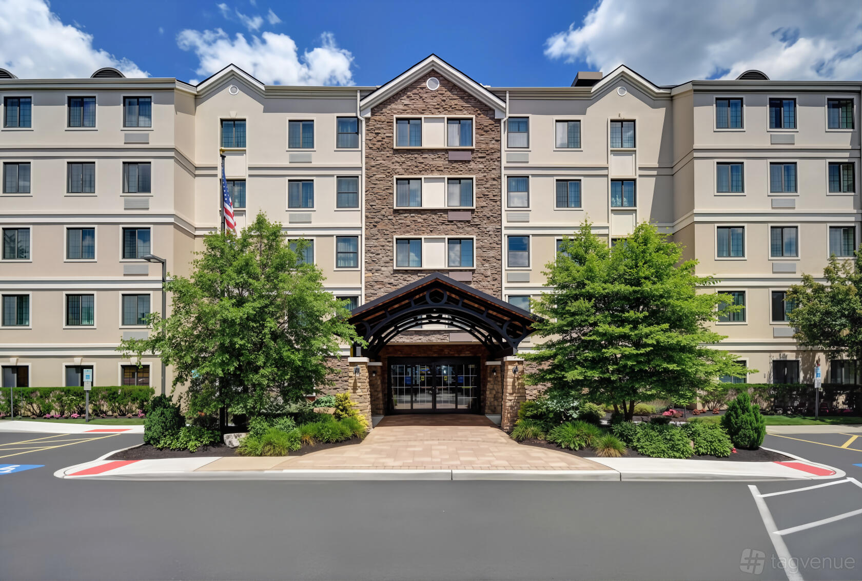 A hotel exterior with a stone entrance, covered driveway, and manicured landscaping at Homewood Suites Eatontown-Tinton Falls.