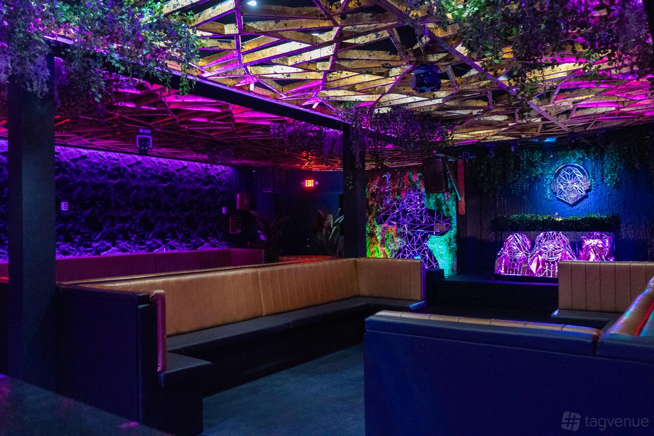 An event venue with built-in tan leather seating, greenery decor, and colorful LED lighting at MAZUMA.