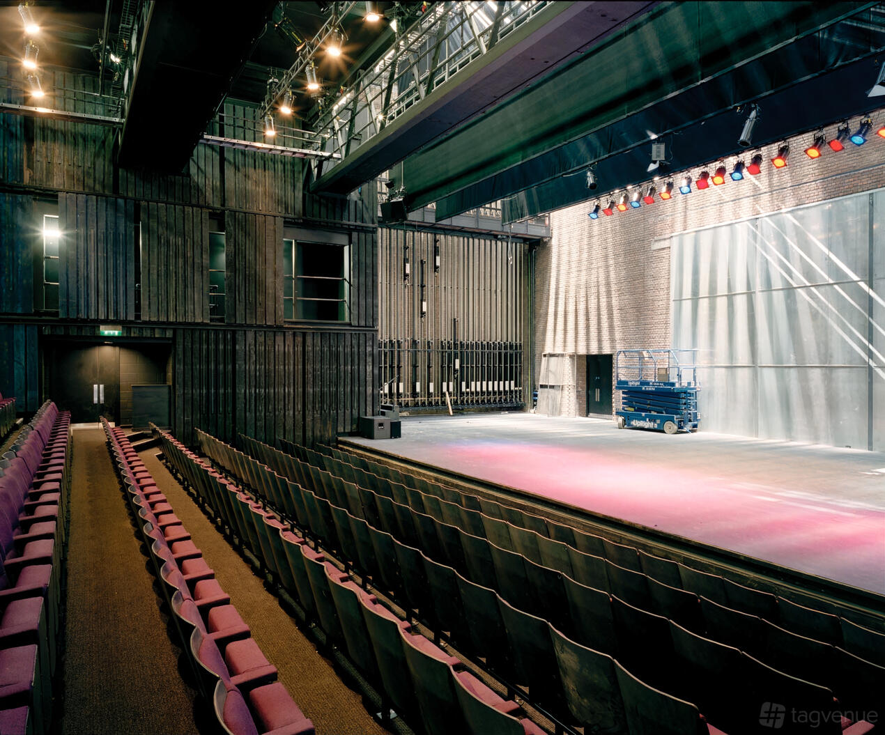 An auditorium with tiered seating, industrial walls, and a stage lit by overhead spotlights at The Northern Stage.