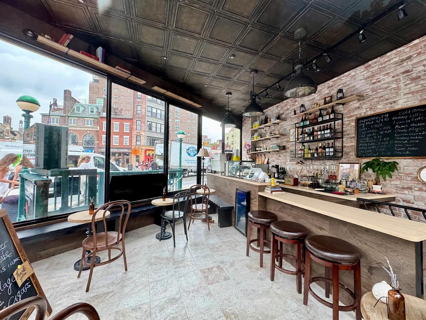 A bar with exposed brick walls, large street-facing windows, wooden stools, and hanging shelves at MAMALI NYC.