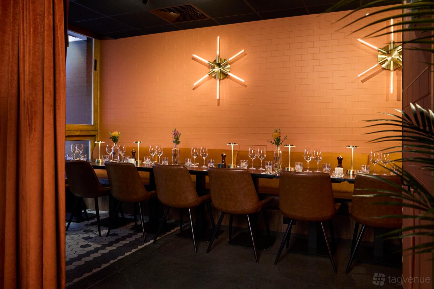An event space with a long dining table, brown upholstered chairs, wall sconces, and set glassware at KöD Soho.