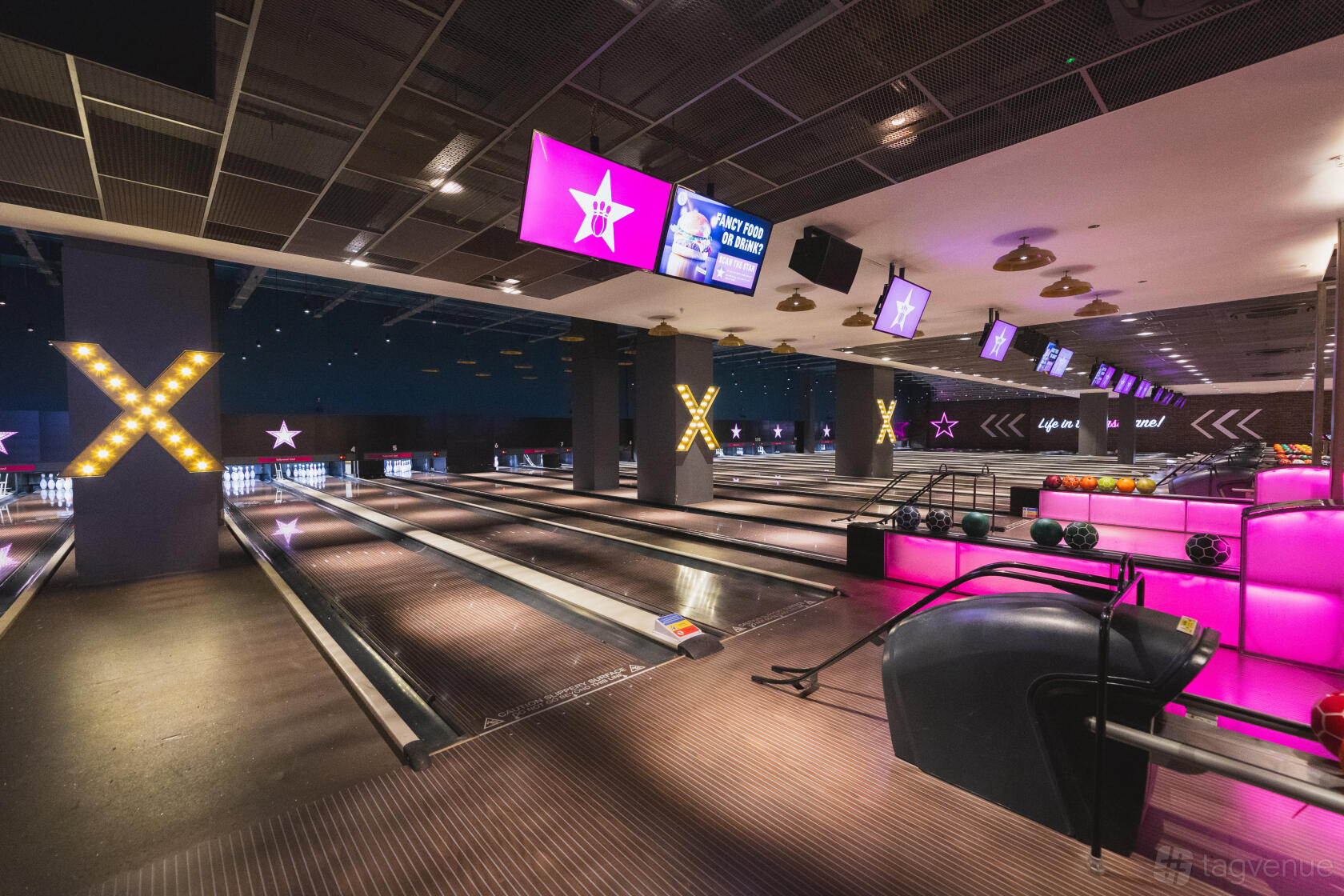 A bowling alley with illuminated lanes, neon pink lighting, and digital scoring screens at Hollywood Bowl Birmingham Resorts World.