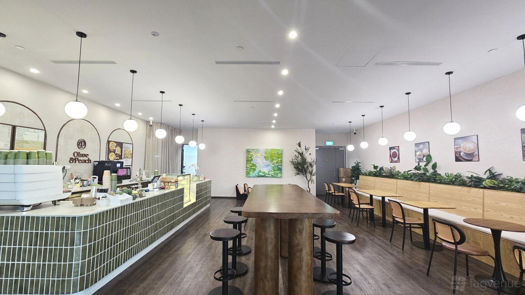 An event space in a cafe with globe pendant lighting, long wooden tables, and green tile counter at Olive & Peach (Kent Ridge).