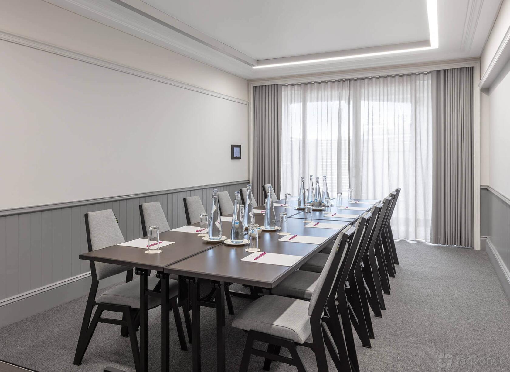 An event space in a hotel with a long meeting table, grey chairs, bottled water, and natural light at Crowne Plaza Terrigal Pacific.