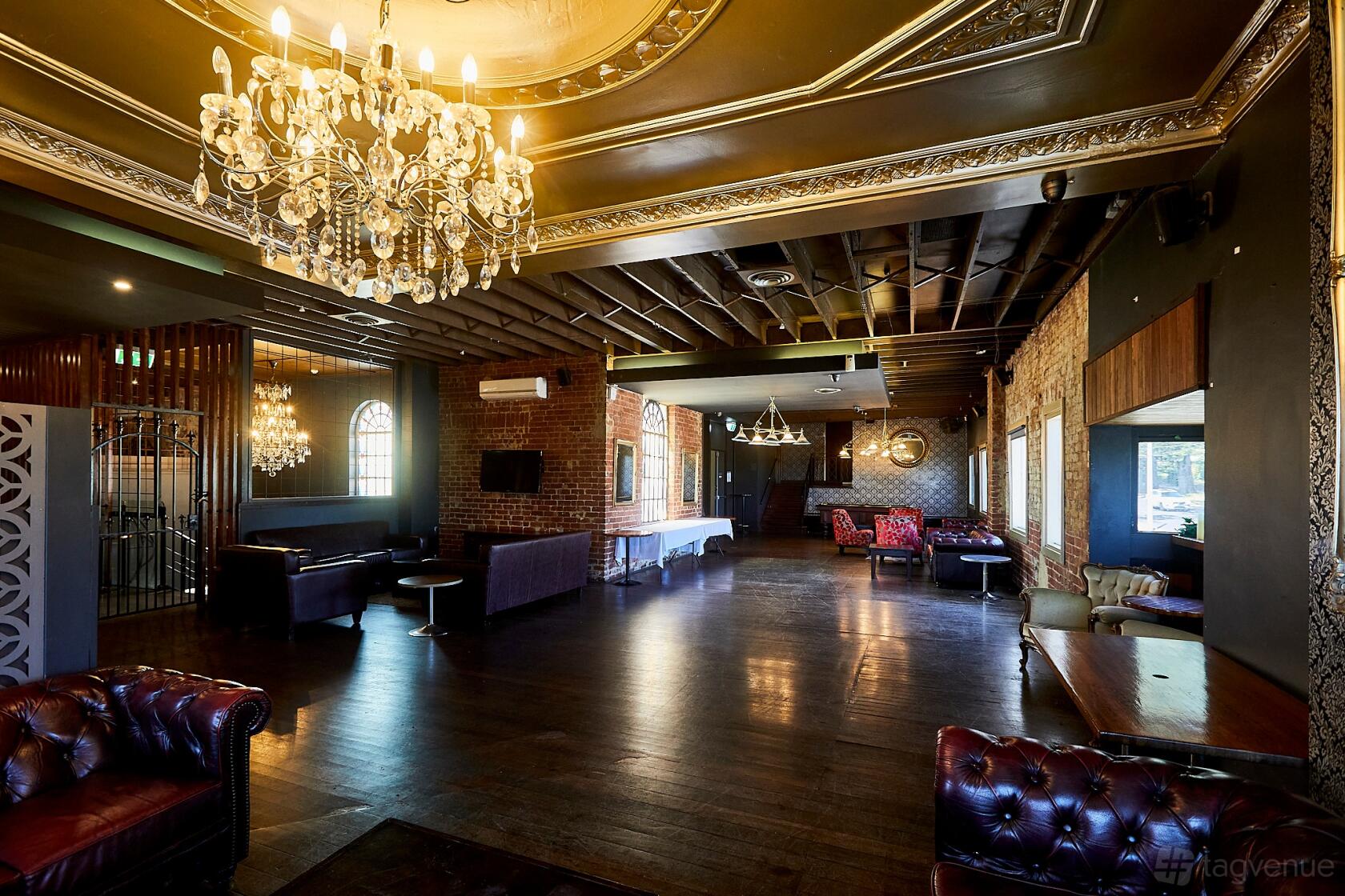 A pub function room with exposed brick walls, chandeliers, leather armchairs, and dark wood floors at The Grand Hotel - Frankston.