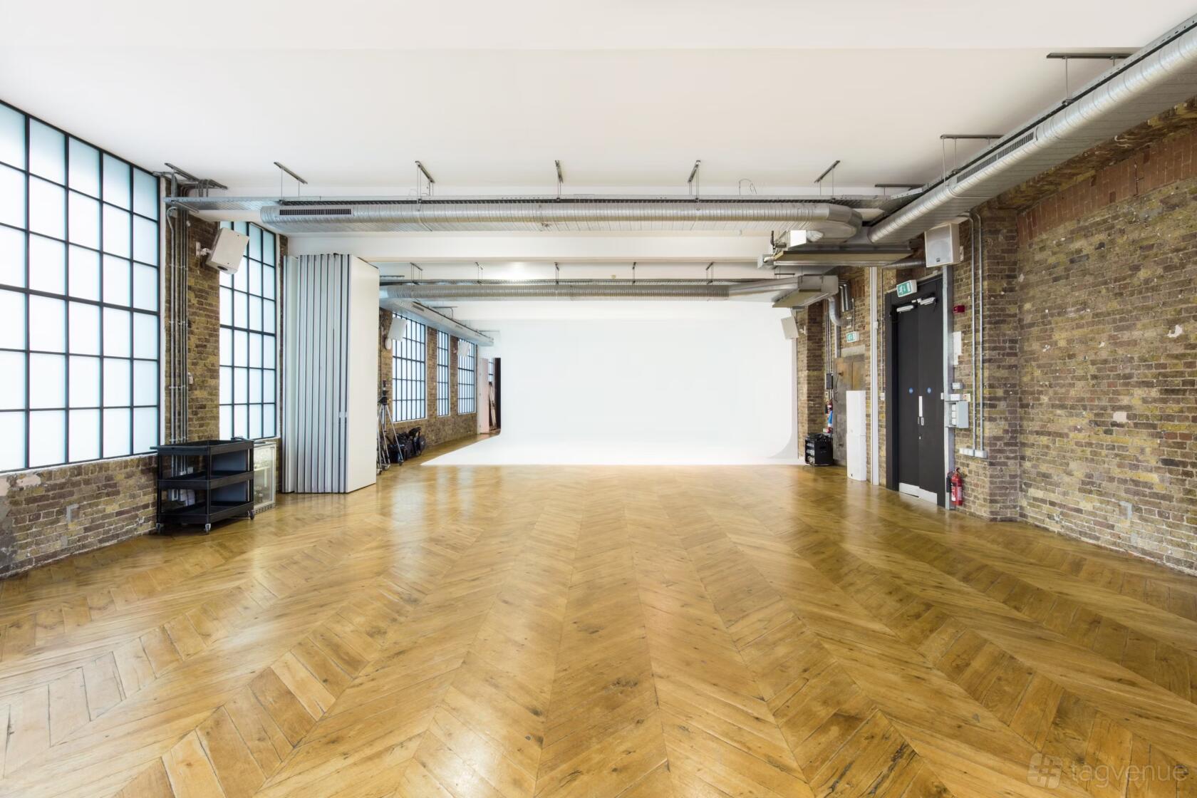 A blank canvas warehouse with herringbone wood flooring, exposed brick walls, and large industrial windows at Spring Studios London.