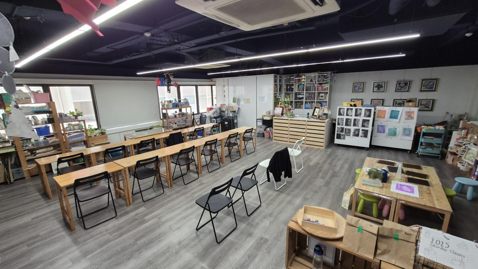 An art studio with long work tables, folding chairs, open shelving, and artwork displayed on the walls at Large Creative Space @ Bugis.