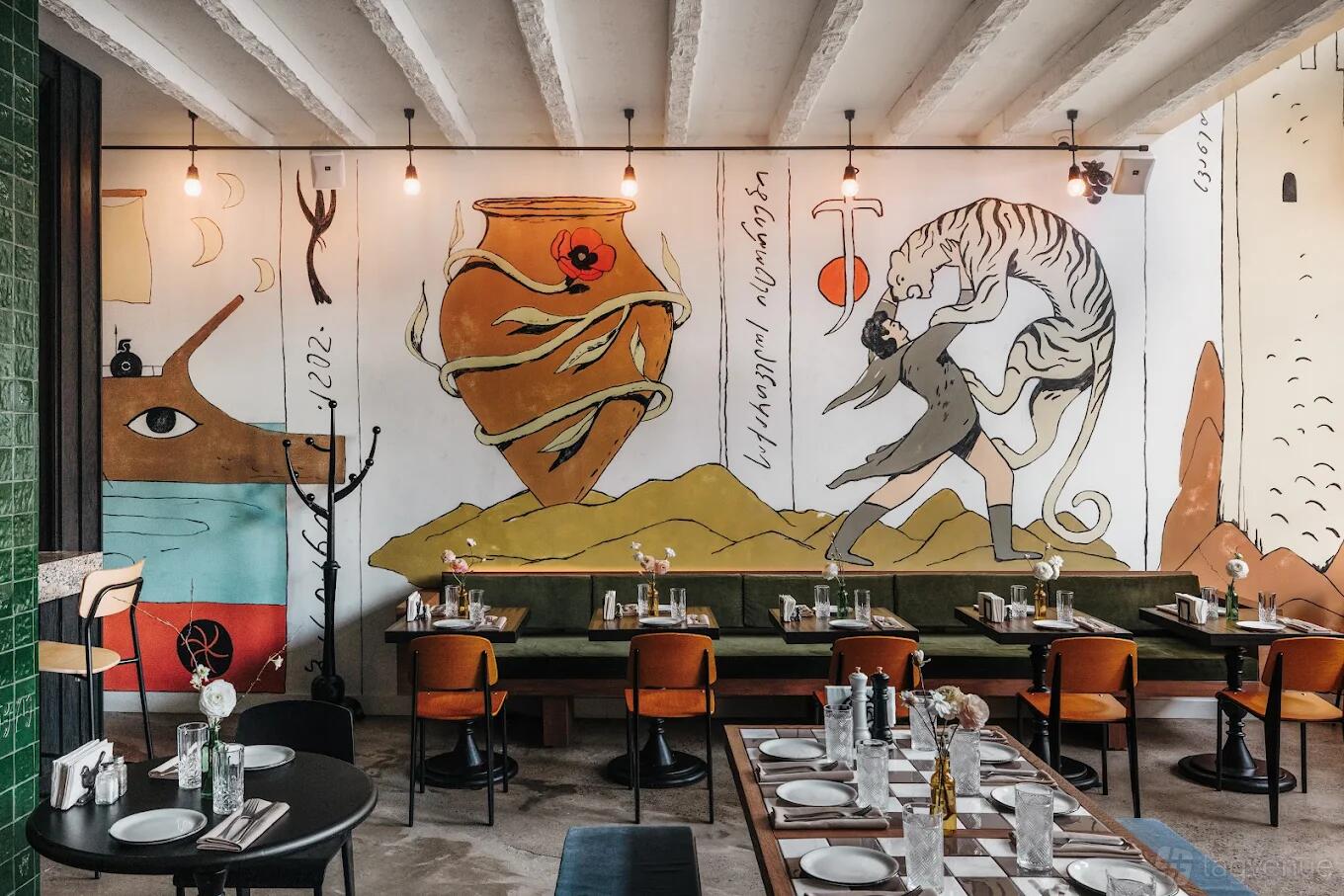 A dining room with colorful mural walls, exposed ceiling beams, and tables set with glassware at LALIKO