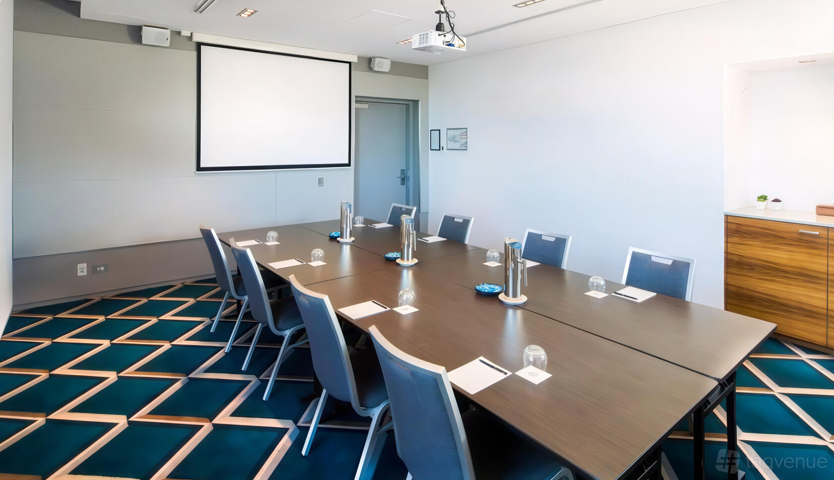 A function room with a long boardroom table, padded chairs, glassware, and a ceiling projector at Pullman Magenta Shores Resort.