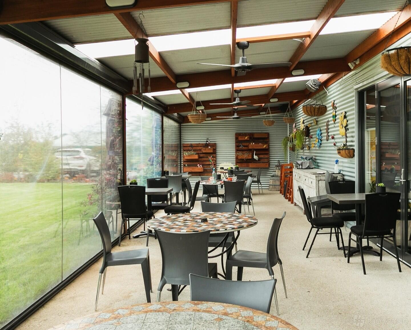 A terrace cafe with round mosaic tables, black chairs, hanging baskets, and corrugated metal walls at Fork N Flower.
